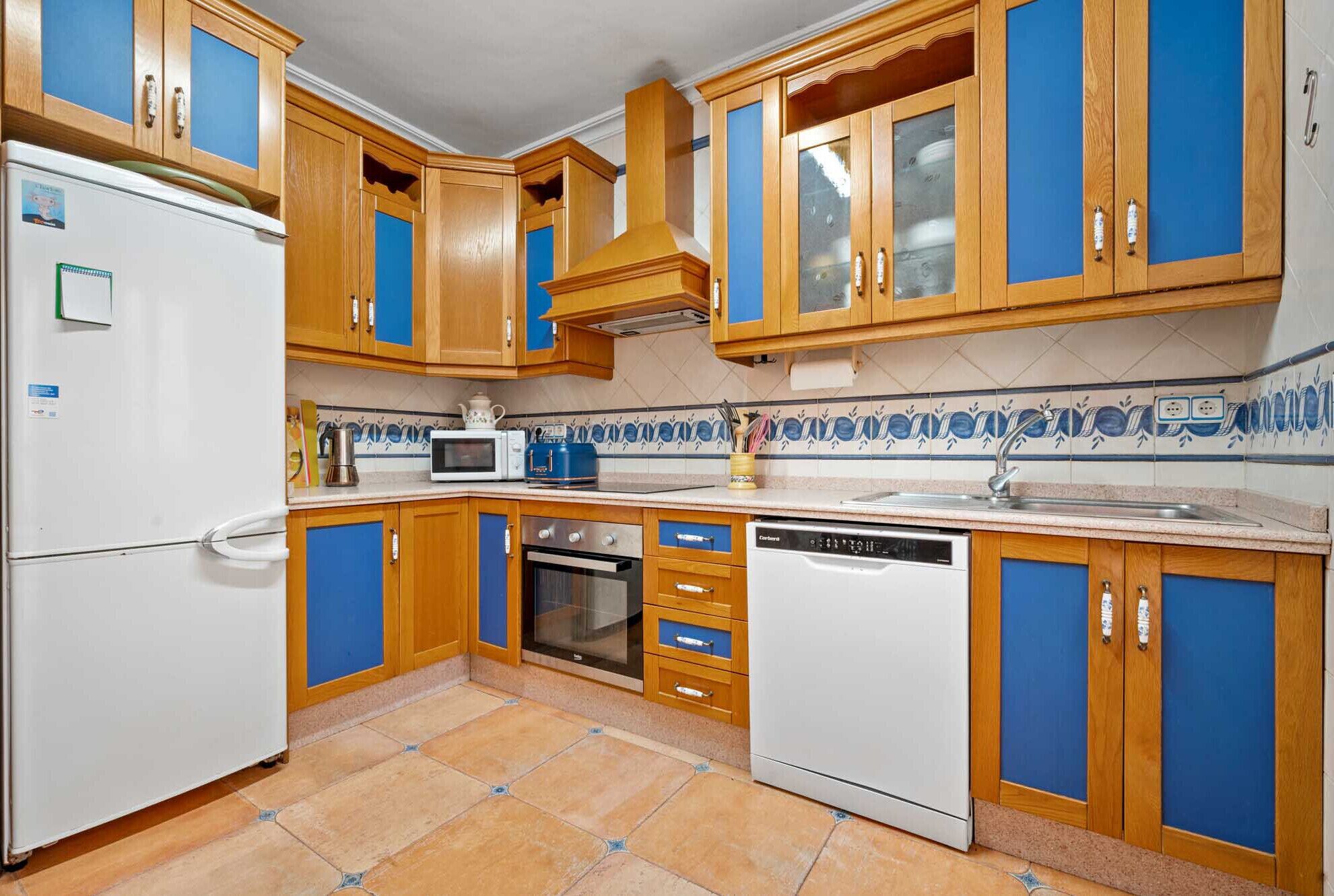 A kitchen with wooden cabinets, a refrigerator, a microwave, a toaster, a dishwasher, and a tiled backsplash.