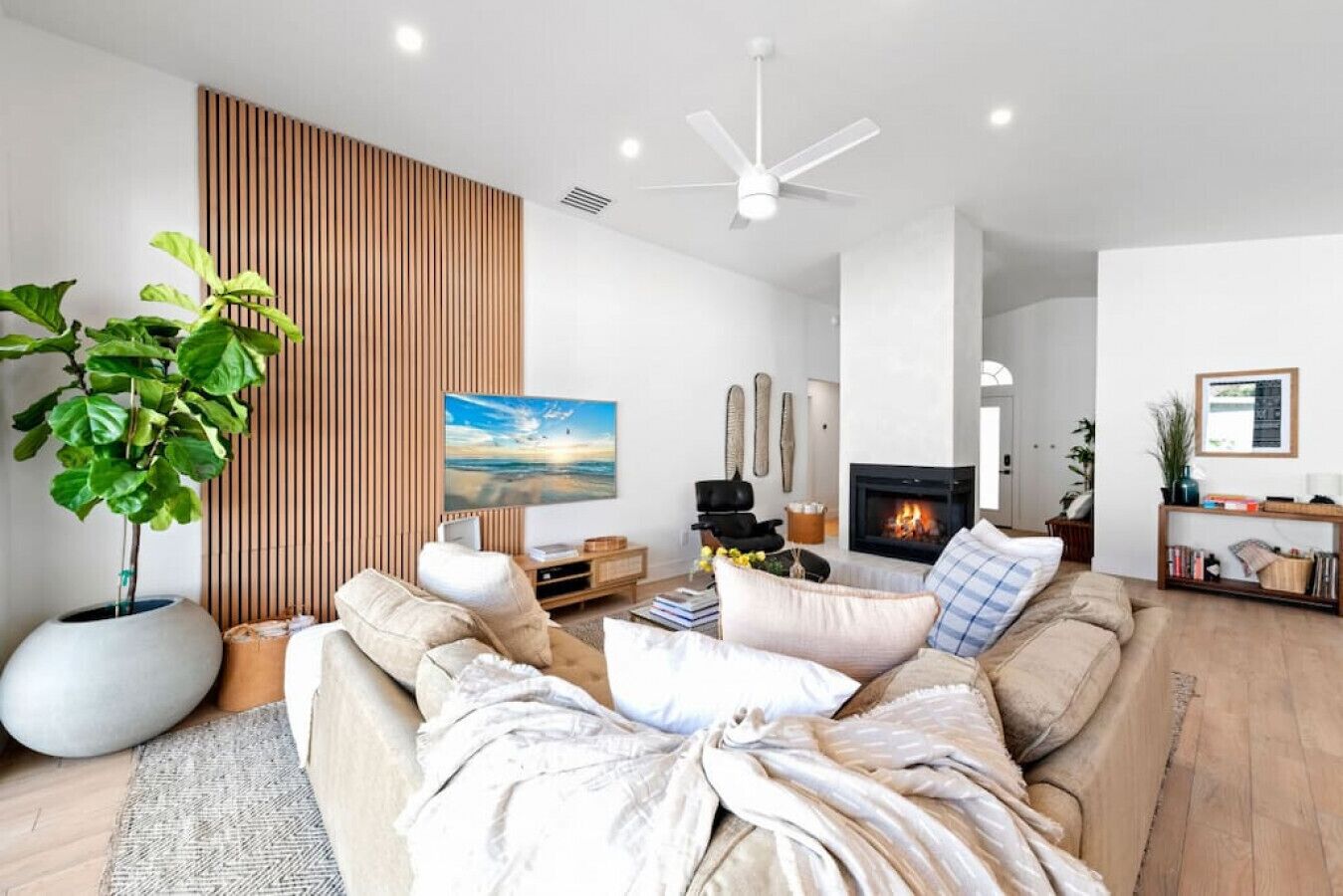 Een moderne woonkamer met een grote bank, een flatscreen televisie, een open haard en een plafondventilator.