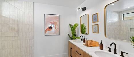 Ein modernes Badezimmer mit zwei Waschbecken, Holzschränken, einem großen Spiegel und einem gerahmten abstrakten Gemälde.