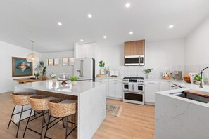 A modern kitchen with white cabinets, a central island with bar stools, a microwave, and a stove.