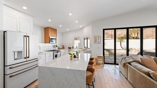 Una cocina moderna con armarios blancos, una isla central y un amplio ventanal con vistas a un jardín.