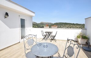 A rooftop terrace with a round metal table and chairs, a potted plant, and a view of a hilly landscape. - Cozy home in Ragusa with WiFi (Ragusa)