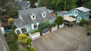 A two-story building with a grey roof, a small porch, and a fenced yard with a sign for 'Enchanted Cottages and Gardens'. - Captain's Cottage – A Unique Vintage stay & Nautical Retreat (Pacific County)