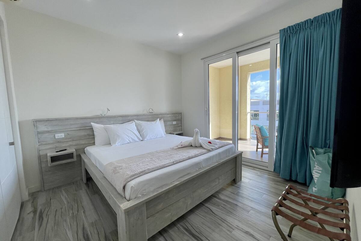 A bedroom with a large bed, a wooden headboard, a small bedside table, and a chair.