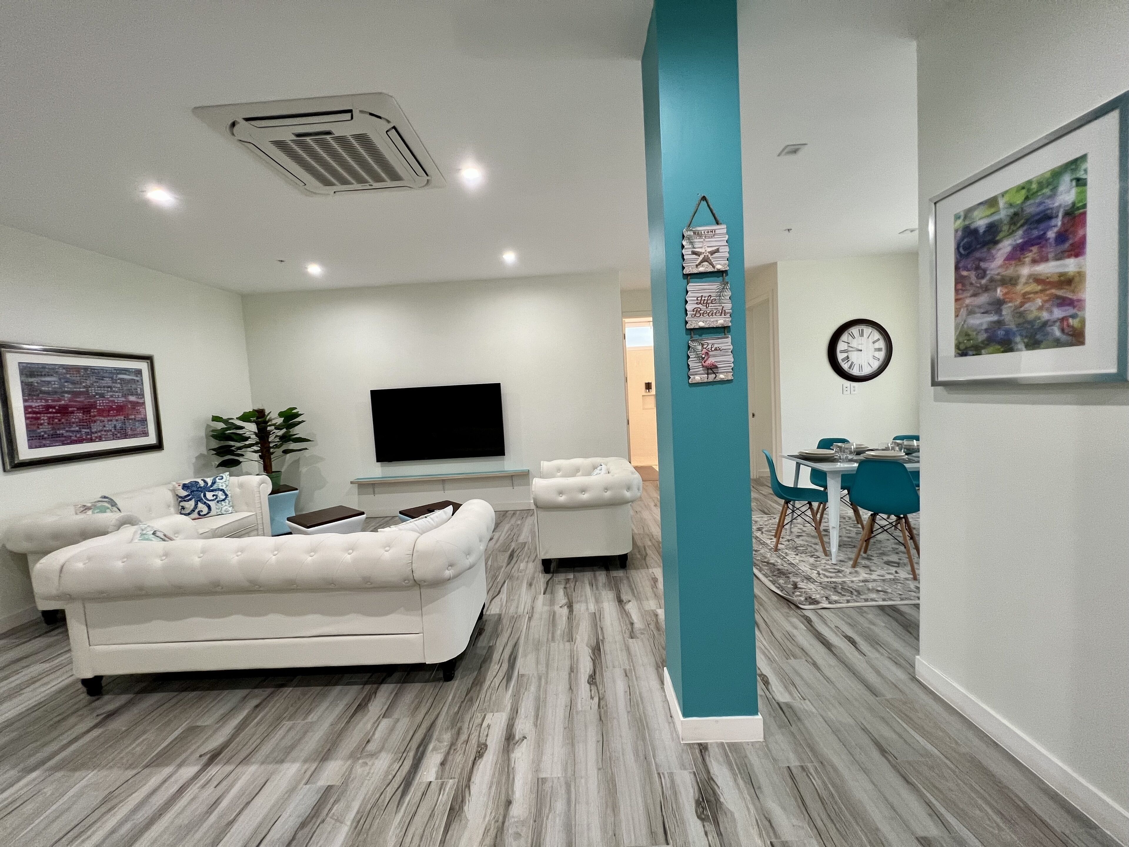 Una sala moderna con un sofá blanco, un televisor de pantalla plana y una pared de acento color turquesa.