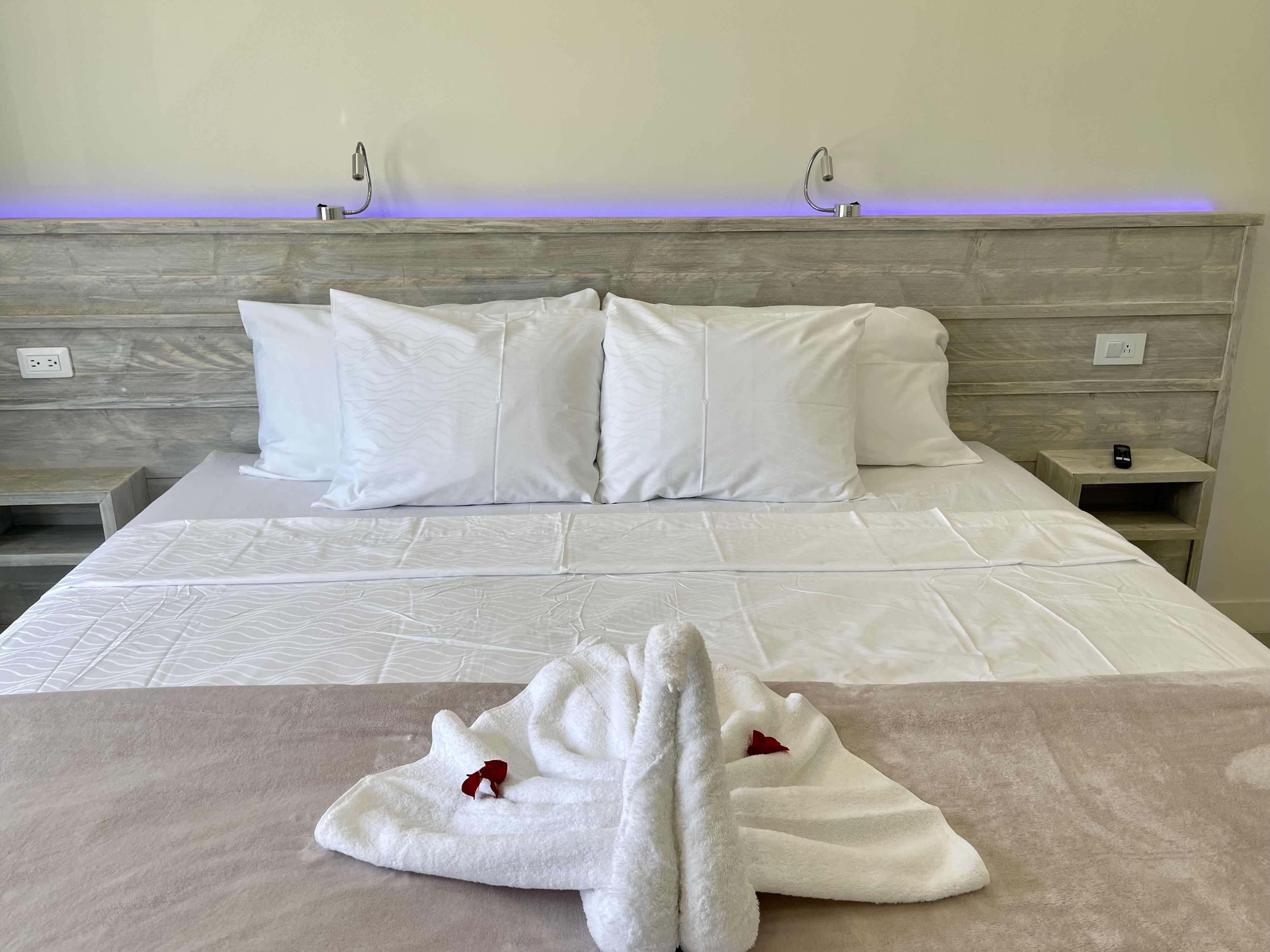 Un lit bien fait, avec du linge de lit blanc et des oreillers, une tête de lit en bois et une table de chevet avec une horloge.