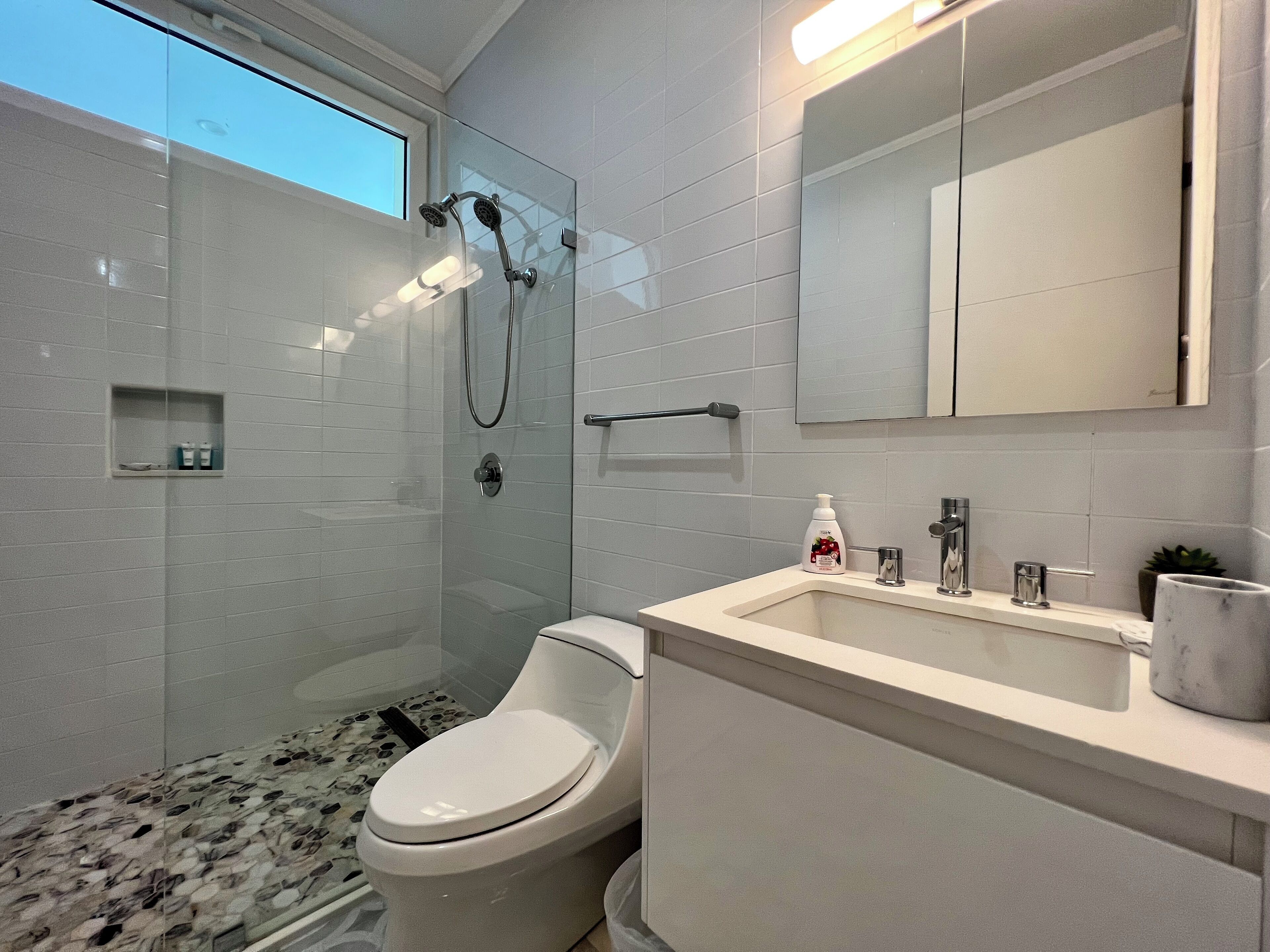 A modern bathroom with a glass shower enclosure, a toilet, a sink with a marble countertop, and a large mirror above the sink.