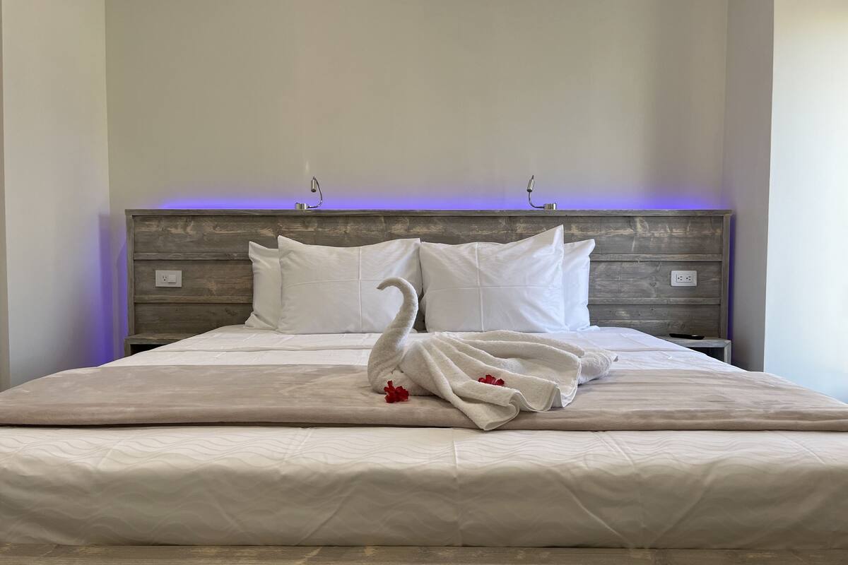 A neatly made bed with white linens and a swan-shaped towel arrangement.