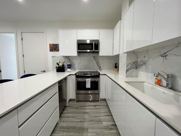 Uma cozinha moderna com armários brancos, forno de aço inoxidável e painel de fundo de mármore.