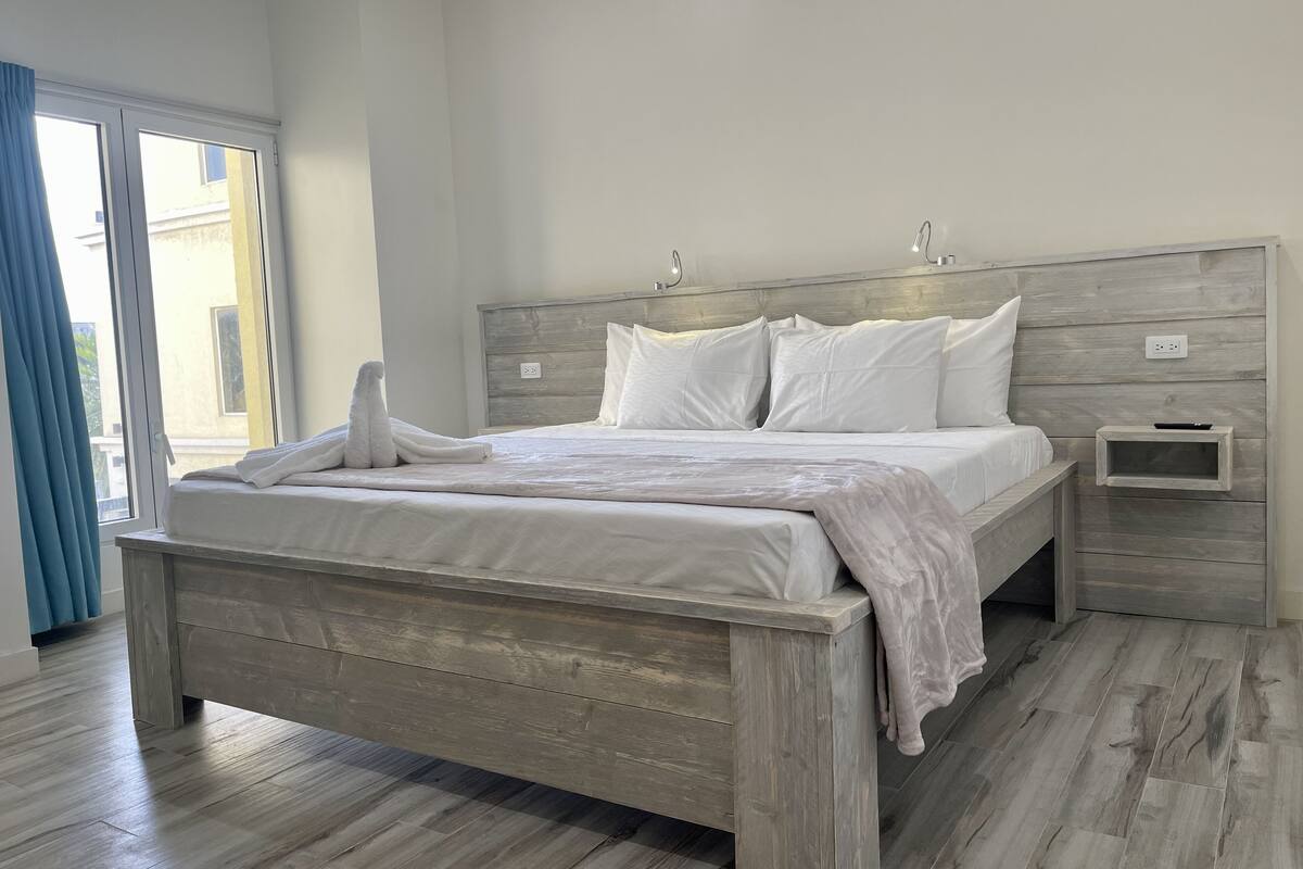 A modern bedroom with a wooden bed frame, white bedding, and a nightstand with a remote control.