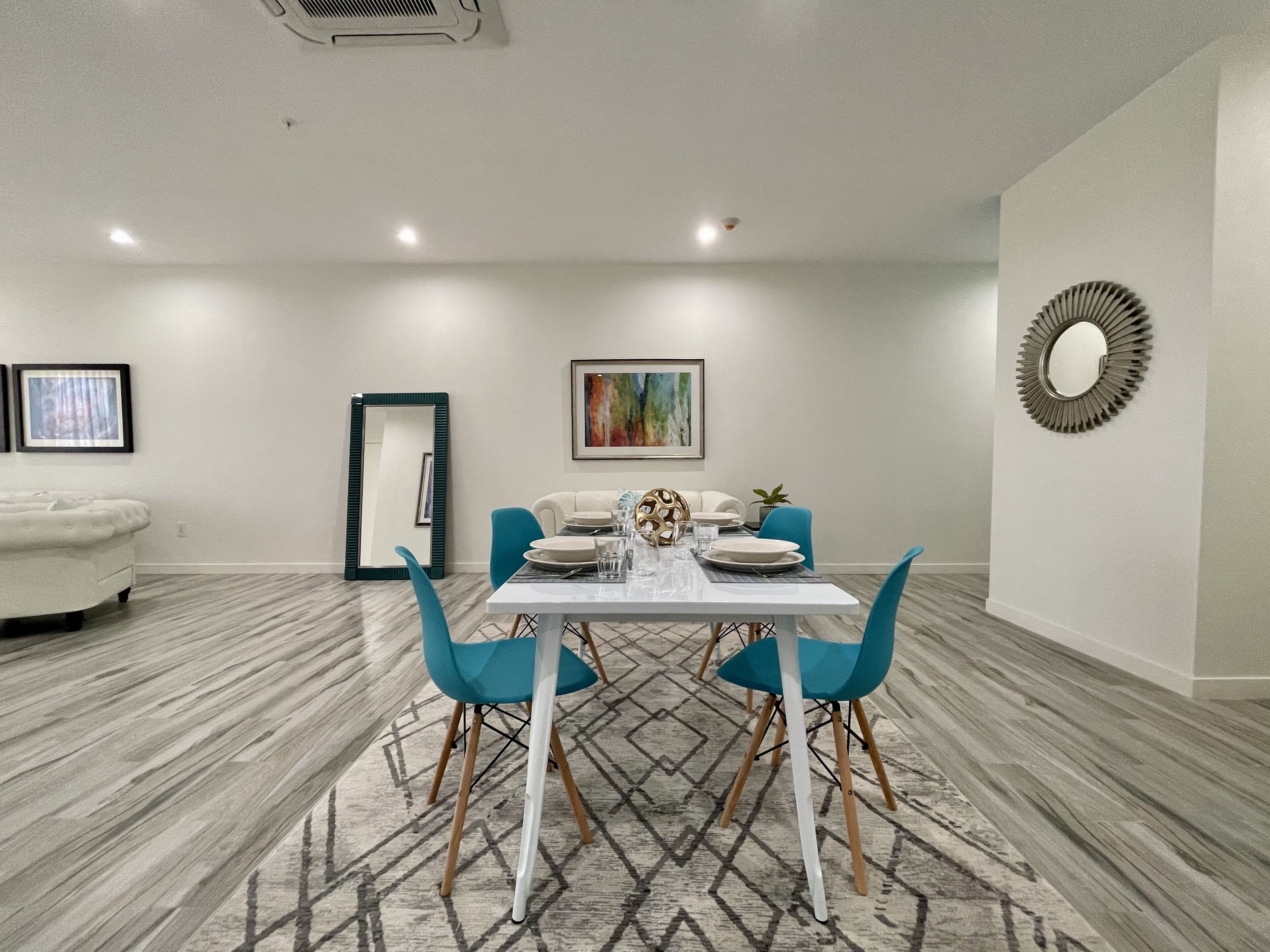 Un coin repas avec une table blanche, des chaises bleues et un tapis à motifs.