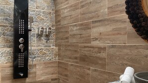A shower area with a black rain showerhead, stone and wood wall tiles, and a pine cone decoration.