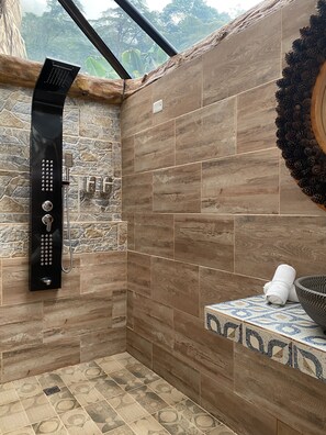 A shower area with a black rain showerhead, stone and wood wall tiles, and a pine cone decoration.