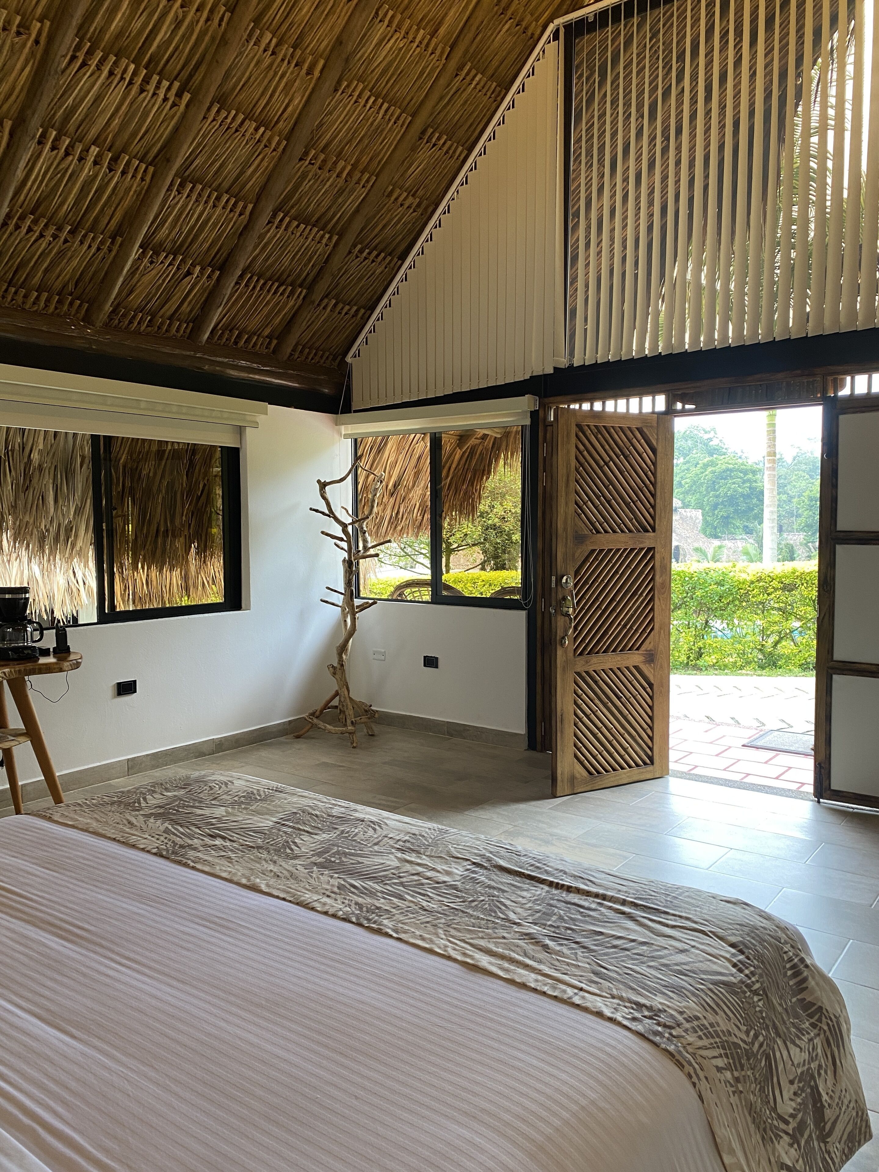 Un dormitorio con una cama grande, techo de madera y vistas a un jardín a través de puertas abiertas.