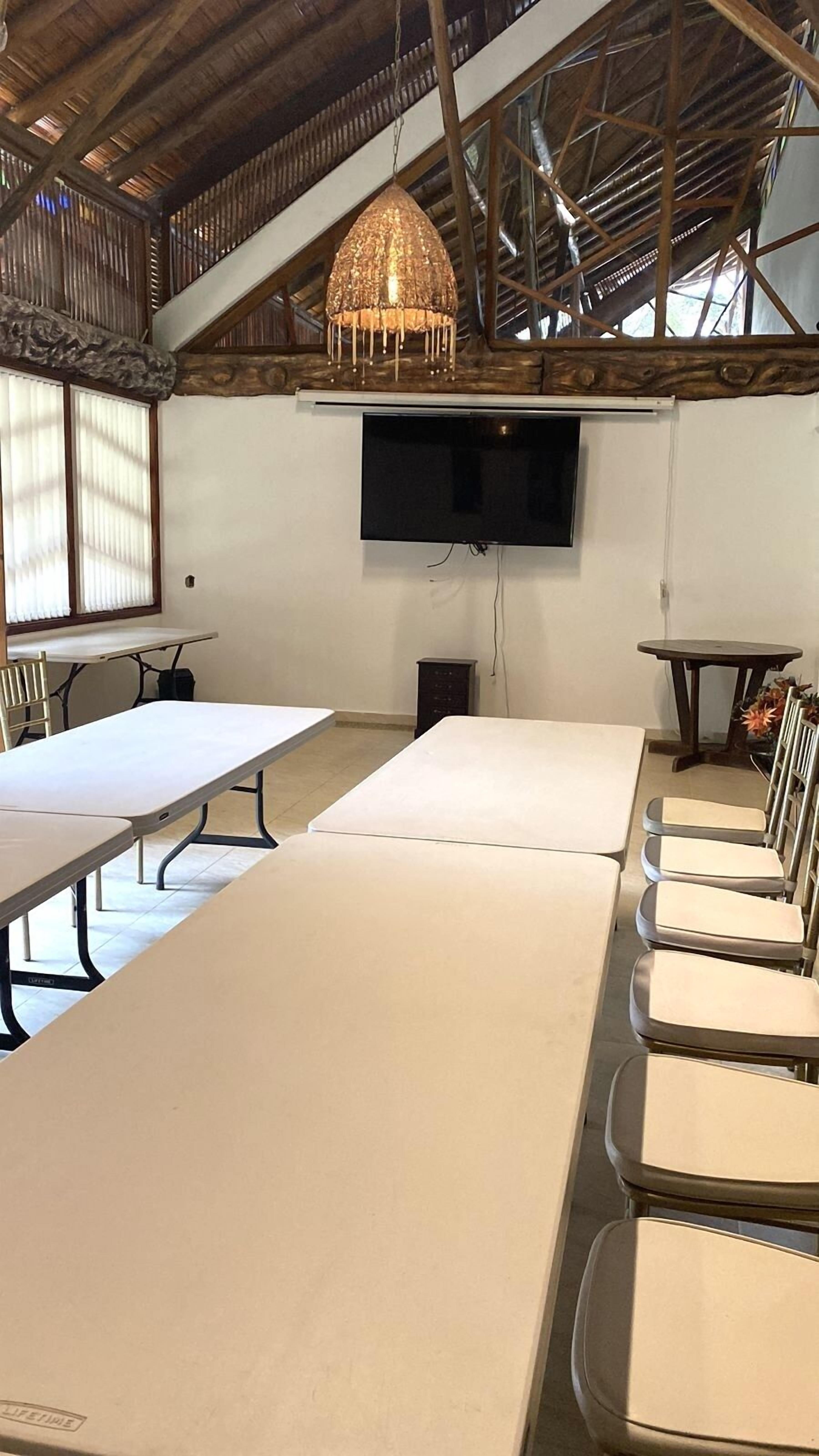 A conference room with long tables and chairs, a flat-screen TV mounted on the wall, and a rustic ceiling with exposed beams.