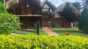 A wooden house with thatched roofs, a checkered pathway, and well-maintained greenery.