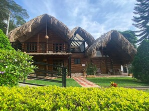 A wooden house with thatched roofs, a checkered pathway, and well-maintained greenery.
