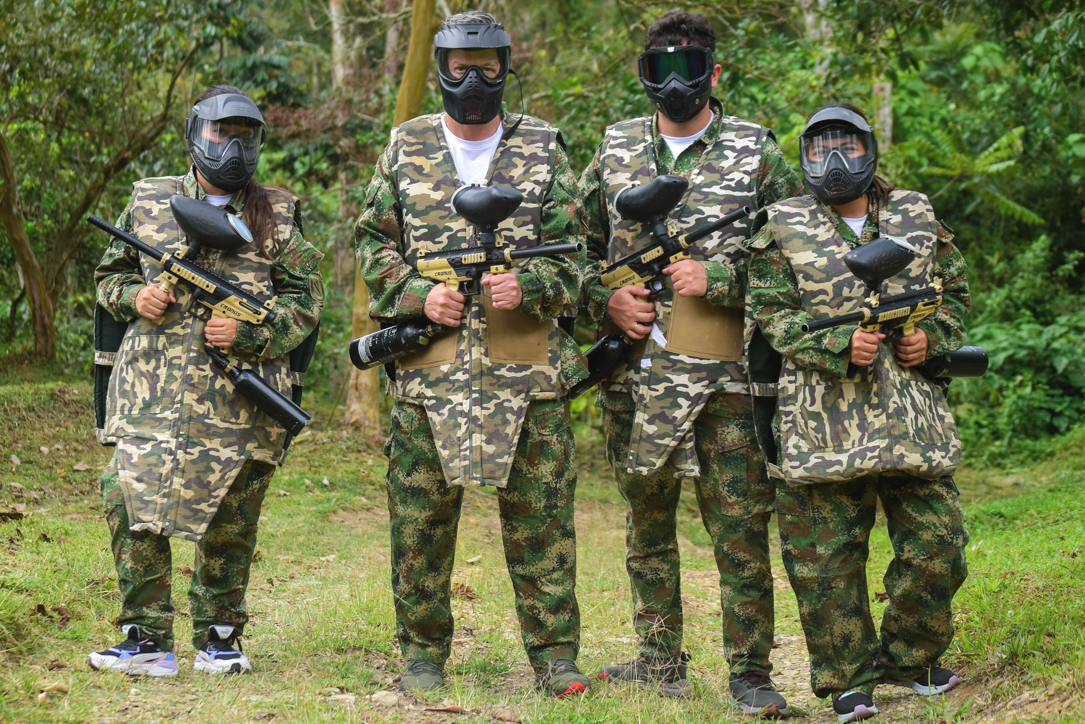 Quatro pessoas em uniformes de camuflagem segurando armas de paintball, em uma área externa gramada.