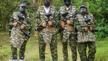 Quatro pessoas em uniformes de camuflagem segurando armas de paintball, em uma área externa gramada.