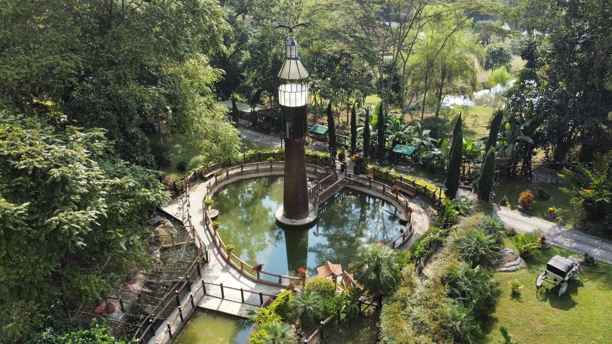 Una fuente circular con una torre central, rodeada por una terraza de madera y exuberante vegetación.
