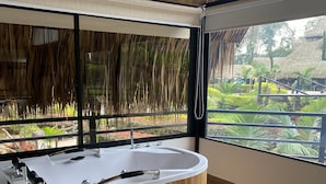 Een moderne badkamer met een vrijstaand bad, grote ramen en uitzicht op een tropische tuin.