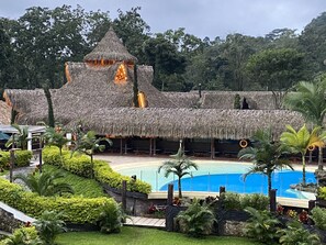 A resort with a thatched-roof building, a swimming pool, and lush greenery.