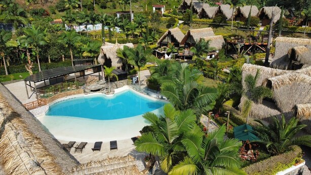Een resort met een centraal gelegen zwembad, rieten hutten en weelderige tropische begroeiing.