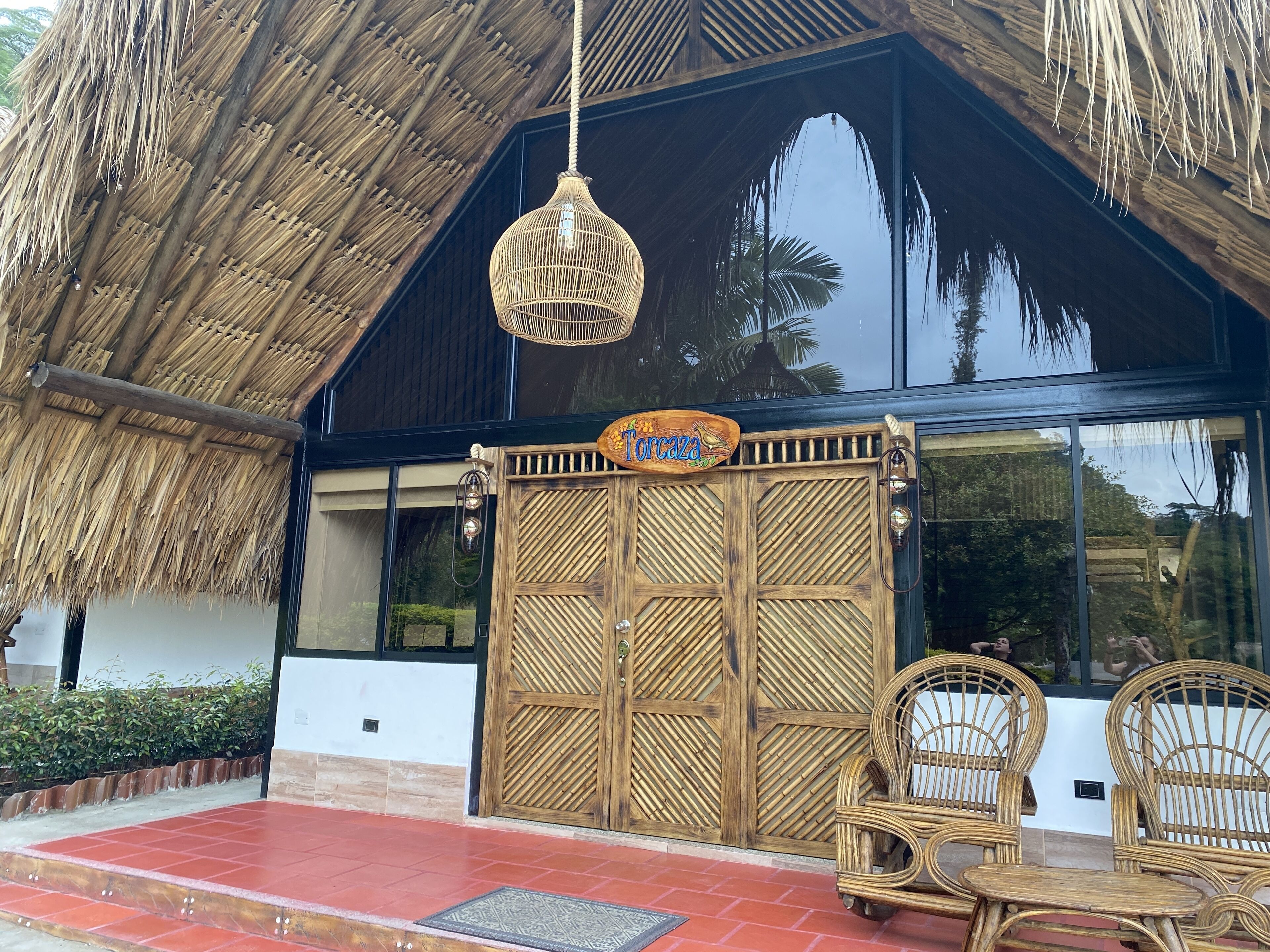 Un edificio con techo de paja, un portón de madera y dos sillas de mimbre en el exterior.