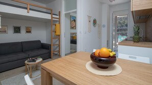 Un salon moderne avec un canapé gris, une table en bois sur laquelle se trouve un panier de fruits, et une vue sur une piscine à travers une porte vitrée.
