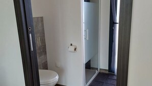 Um banheiro moderno com vaso sanitário, box de vidro e piso de madeira escura.