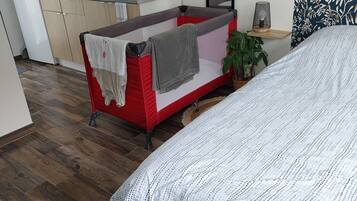 A compact bedroom with a bed, a small bedside table with a lamp, and a kitchenette in the background.