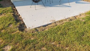 Um edifício moderno com telhado plano, uma grande porta de vidro deslizante e uma área de pátio com duas cadeiras de metal preto e uma pequena mesa redonda.