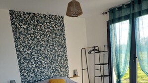 Quarto com cama, escrivaninha, cadeira, luminária pendente e janela com cortinas.