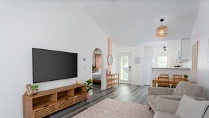 A modern living room with a flat-screen TV, wooden entertainment unit, beige sofa, and a patterned rug. - Quiet Boho Townhouse; 15 Min to Beach (Wilmington)