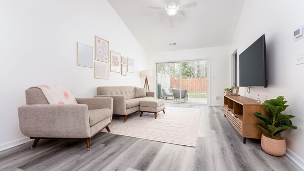 A living room with a sectional sofa, a TV mounted on the wall, and a wooden entertainment unit. - Quiet Boho Townhouse; 15 Min to Beach (Wilmington)