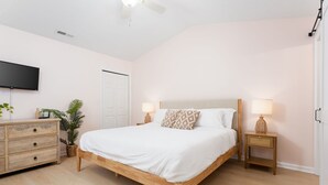 A bedroom with a wooden bed, bedside lamps, a dresser, a television, and a potted plant. - Quiet Boho Townhouse; 15 Min to Beach (Wilmington)