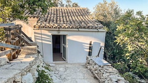 Un bâtiment rustique en pierre, doté d’un toit en tuiles, d’un escalier en bois et d’un chemin en pierre menant à l’entrée.