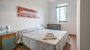 Une chambre à coucher avec un lit, une table de chevet, une commode, une fenêtre et un tableau accroché au mur.
