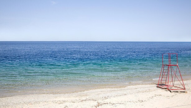 Une plage avec une eau d’un bleu limpide et un poste de surveillance rouge sur le sable.