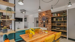 Una sala moderna con una mesa de comedor de madera, sillas amarillas, un muro de ladrillo como detalle y una estantería llena de libros y objetos decorativos.
