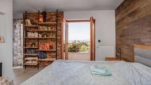 Un dormitorio con una cama grande, una estantería de ladrillo, vistas a través de una puerta abierta y un cabecero de madera.