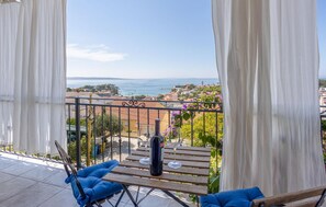 Een balkon met een tafel, twee stoelen en een fles wijn. Het balkon heeft uitzicht op een kustplaats met gebouwen en de zee.