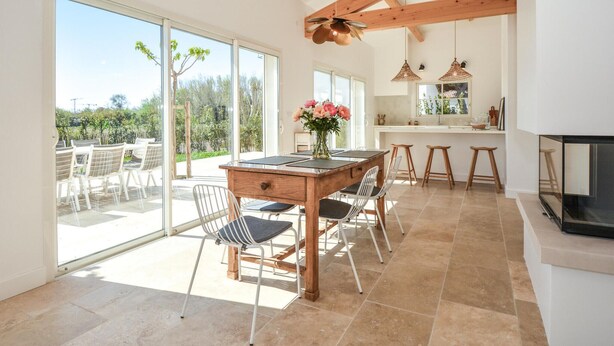 A spacious dining area with a wooden table and chairs, a kitchen with a bar, and large sliding glass doors leading to an outdoor patio. - Amazing home in Serignan (Serignan)
