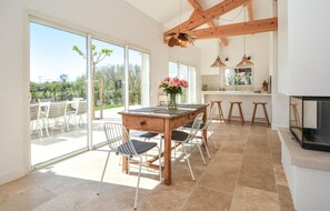 A spacious dining area with a wooden table and chairs, a kitchen with a bar, and large sliding glass doors leading to an outdoor patio. - Amazing home in Serignan (Serignan)