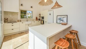 A modern kitchen with white cabinetry, a large island with stools, a window with a view, and pendant lighting. - Amazing home in Serignan (Serignan)