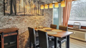 Un'area pranzo con parete in mattoni rustici, un tavolo in legno con quattro sedie e un'ampia finestra vista alberi.
