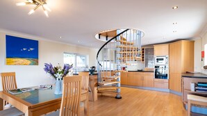 Une cuisine moderne avec un escalier en colimaçon, des meubles en bois et un coin repas comprenant une table et des chaises en verre.