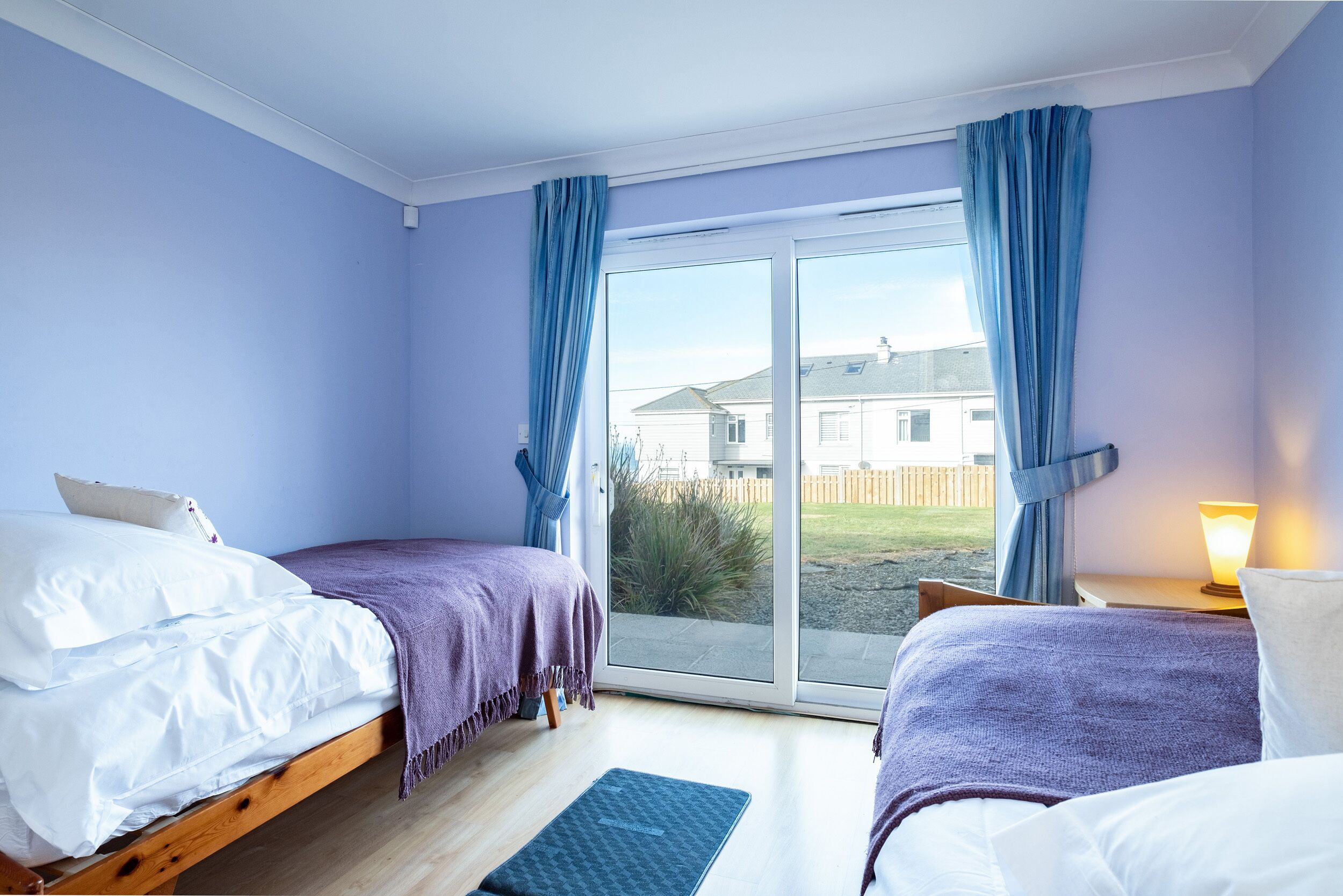 A bedroom with two beds, a sliding glass door to the outside, and a bedside lamp.