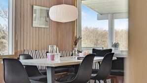 A dining area with a wooden wall, a large window, and a table set with chairs. - 3 bedroom nice home in Løkken (Løkken)