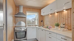 A modern kitchen with wooden paneling, stainless steel appliances, and a window providing natural light. - 3 bedroom nice home in Løkken (Løkken)